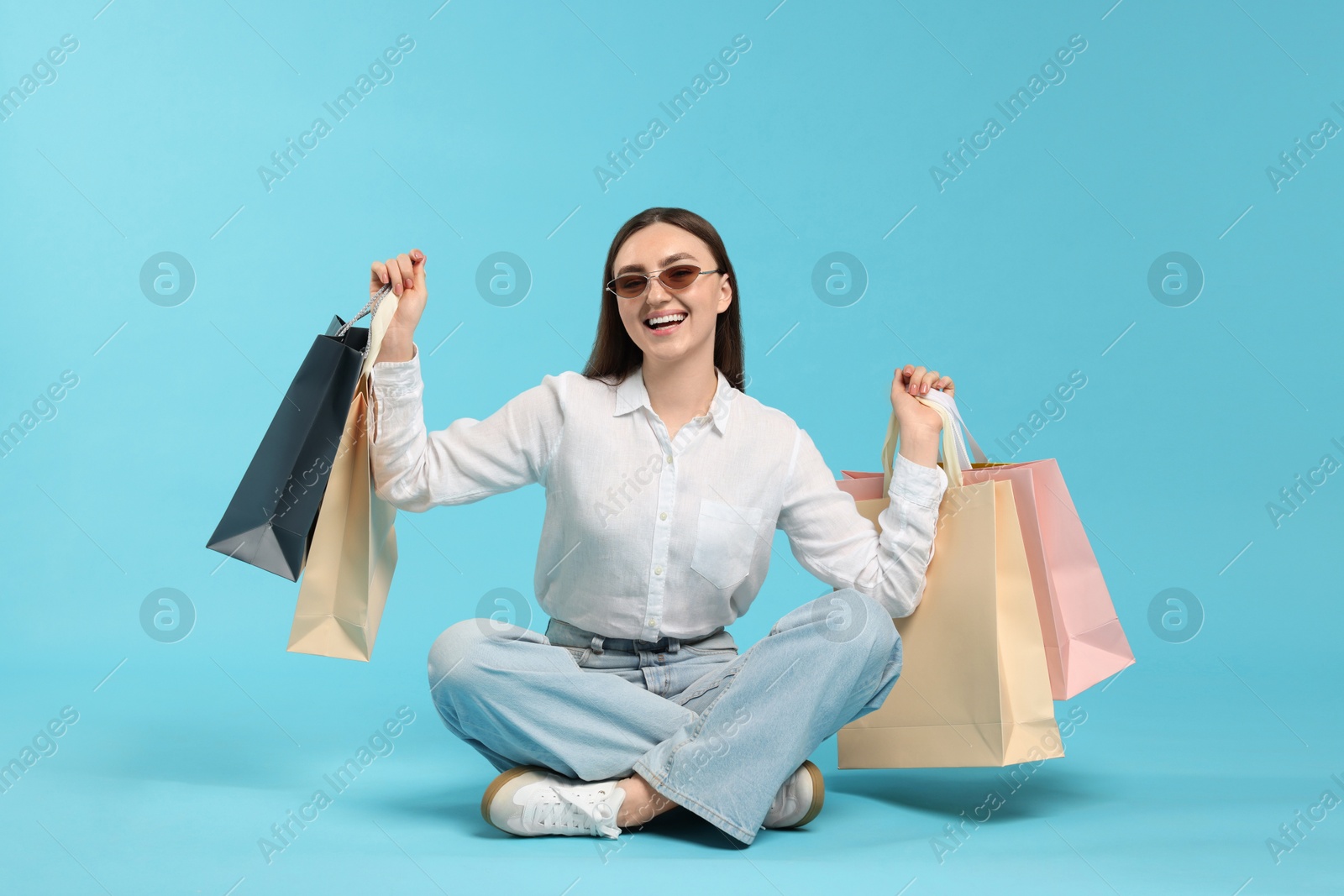 Excited woman with shopping bags on light blue background Photo of Excited woman with shopping bags on light blue background