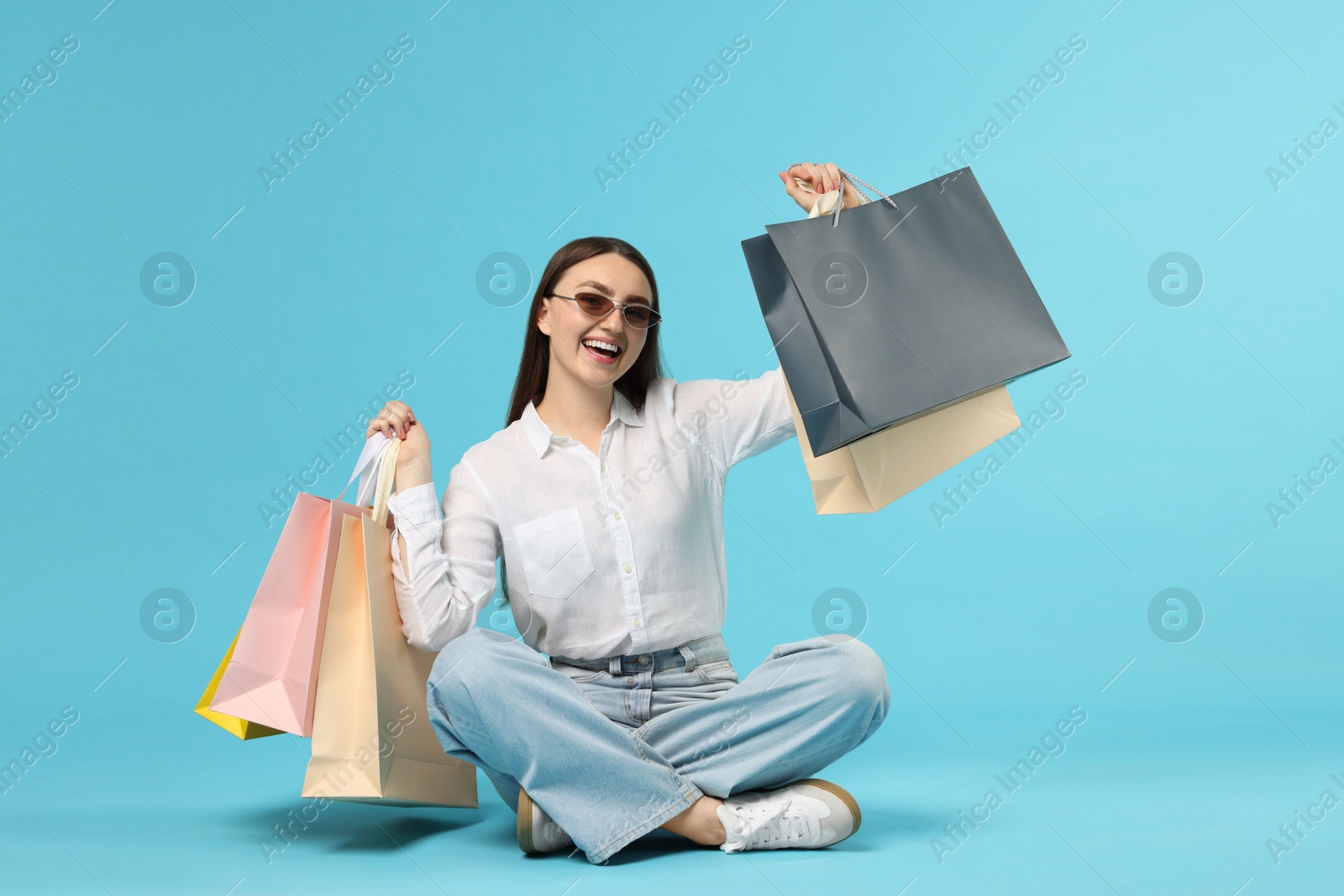 Excited woman with shopping bags on light blue background Photo of Excited woman with shopping bags on light blue background