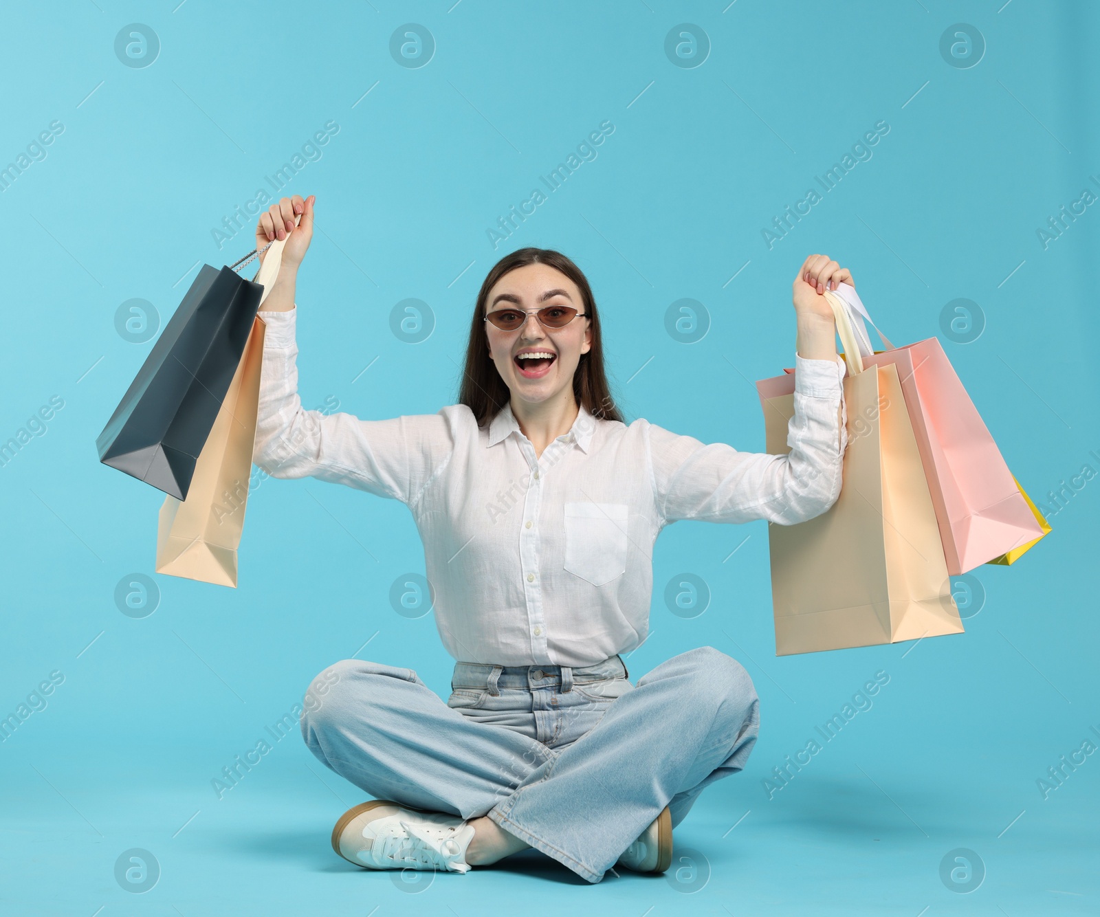 Excited woman with shopping bags on light blue background Photo of Excited woman with shopping bags on light blue background