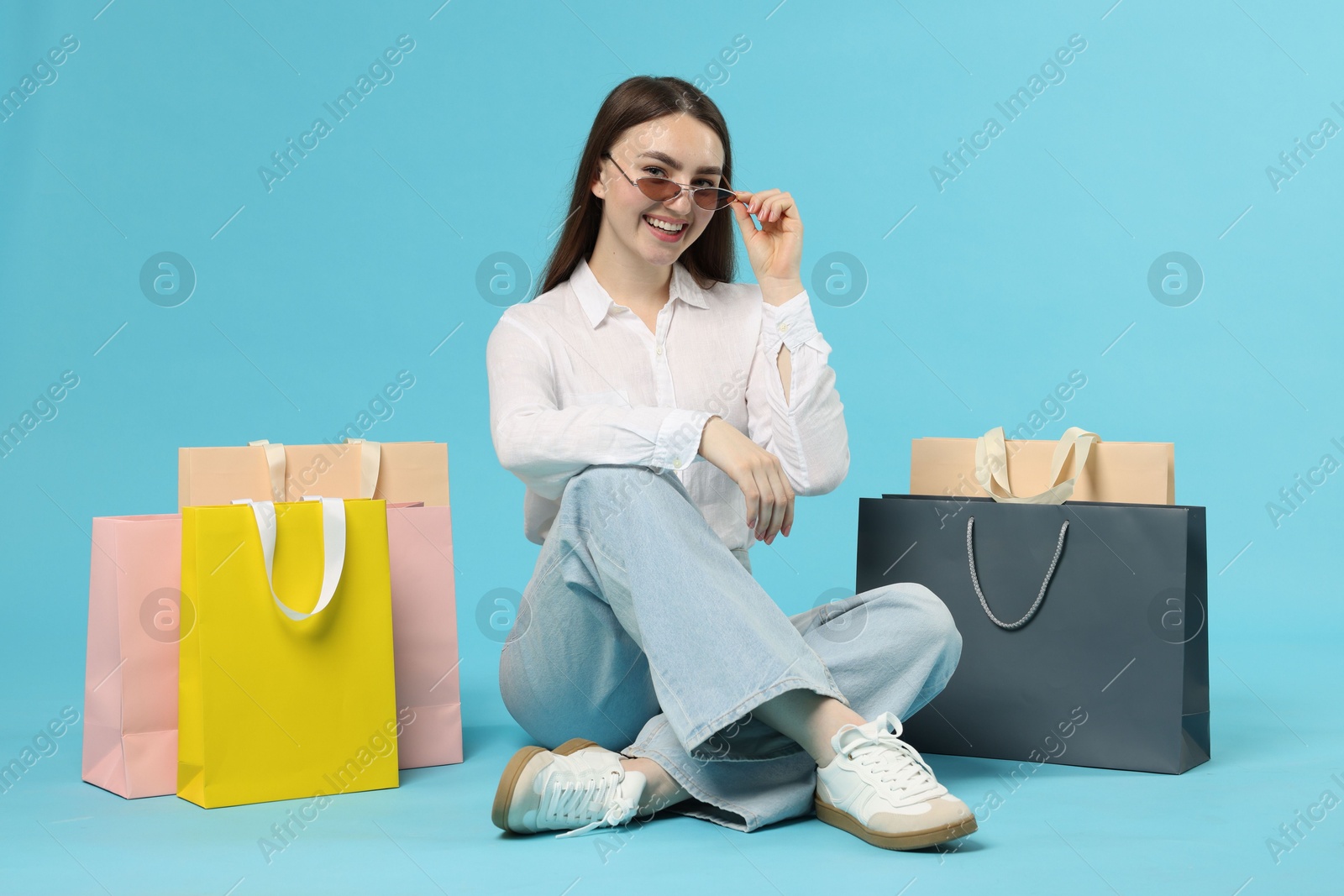 Positive woman with shopping bags on light blue background Photo of Positive woman with shopping bags on light blue background