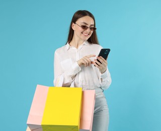 Photo of Positive woman with smartphone and shopping bags on light blue background