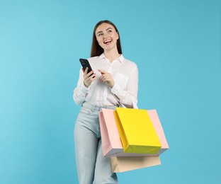 Photo of Positive woman with smartphone and shopping bags on light blue background