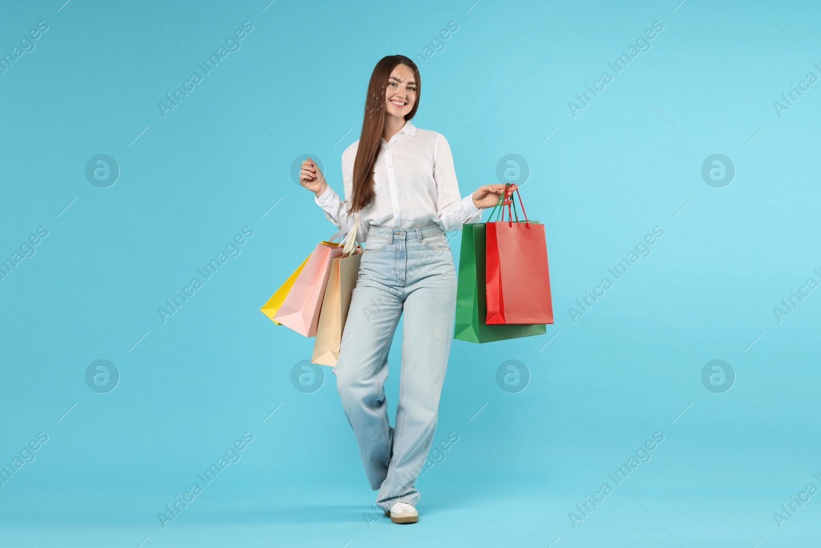 Positive woman with shopping bags on light blue background Photo of Positive woman with shopping bags on light blue background