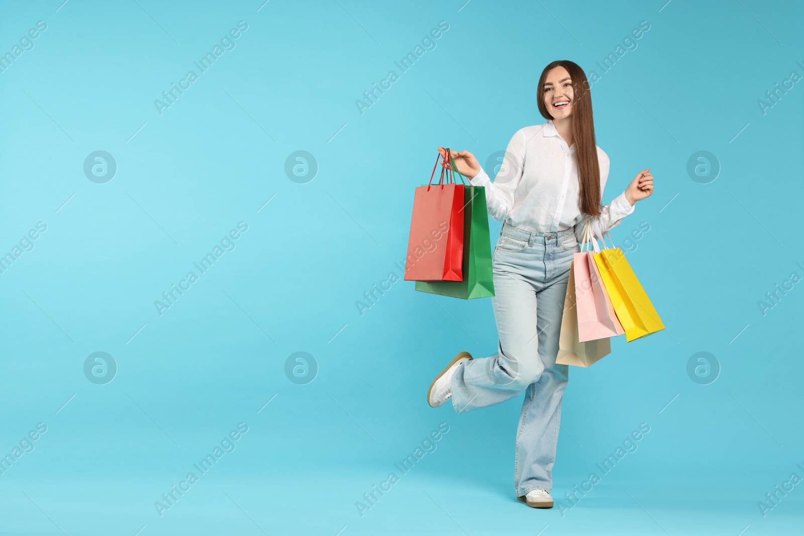 Positive woman with shopping bags on light blue background. Space for text Photo of Positive woman with shopping bags on light blue background. Space for text
