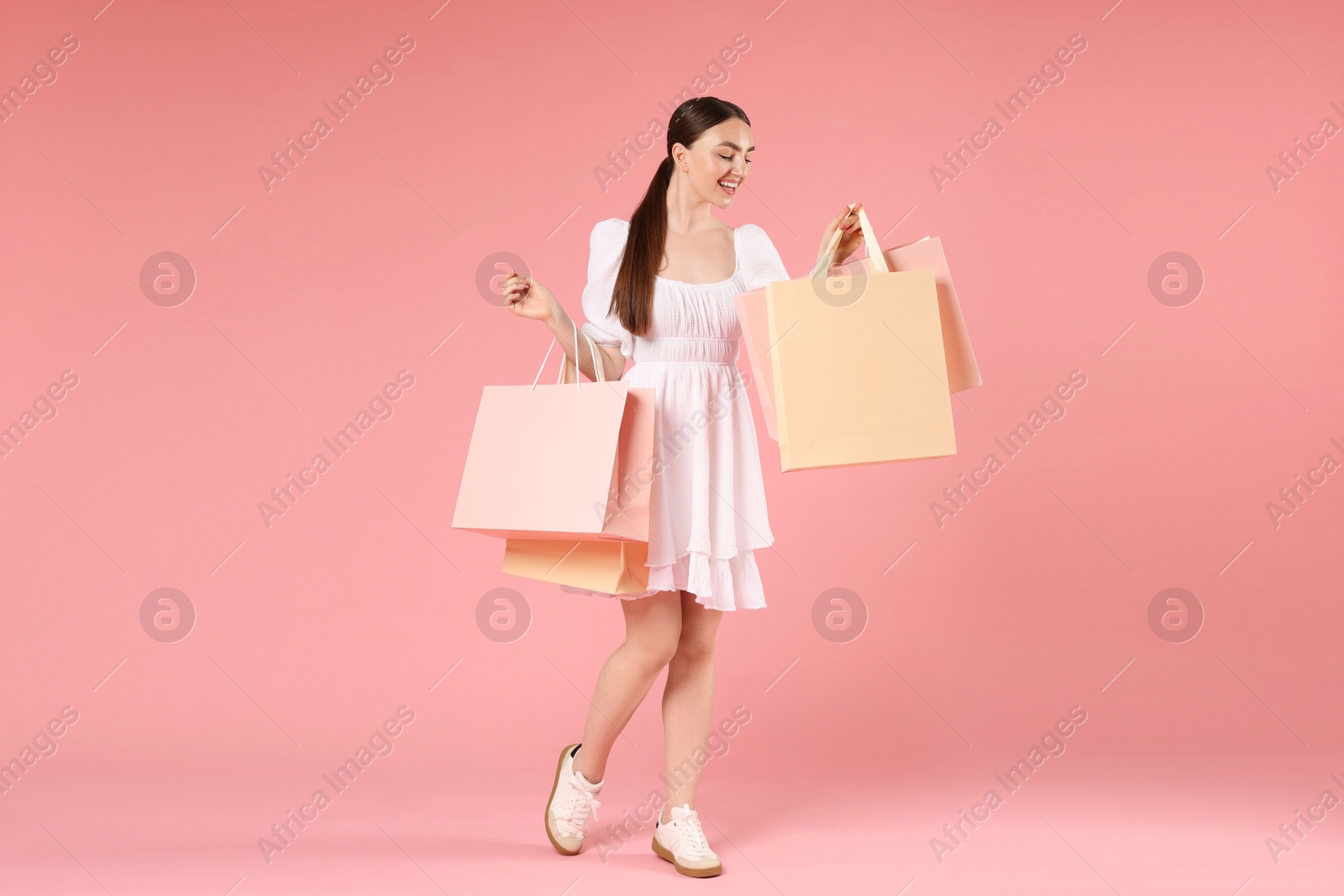 Positive woman with shopping bags on light pink background Photo of Positive woman with shopping bags on light pink background