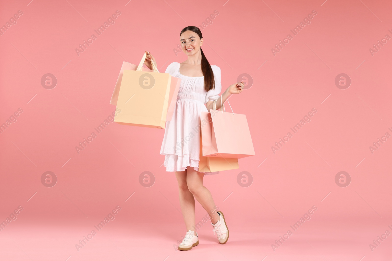 Positive woman with shopping bags on light pink background Photo of Positive woman with shopping bags on light pink background