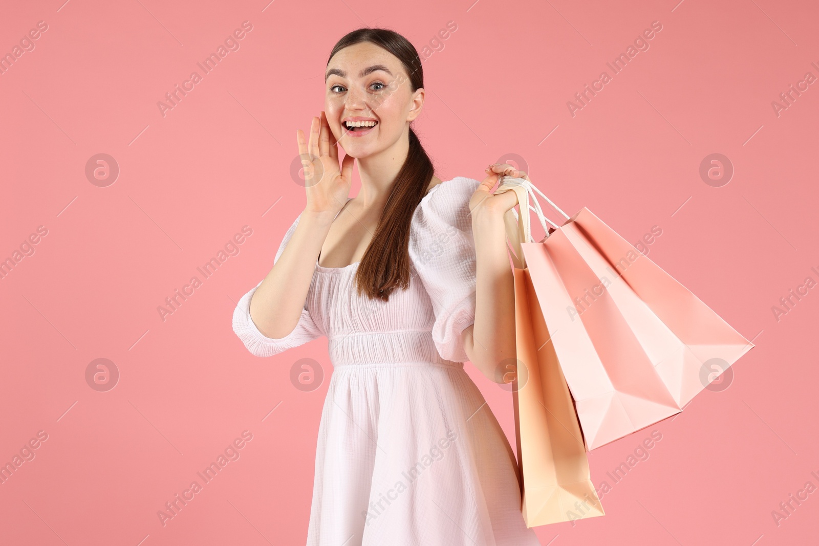 Excited woman with shopping bags on light pink background Photo of Excited woman with shopping bags on light pink background