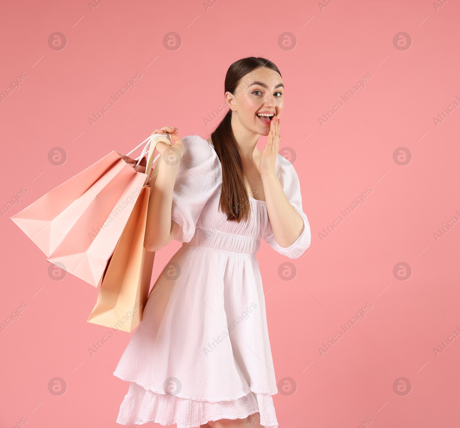 Excited woman with shopping bags on light pink background Photo of Excited woman with shopping bags on light pink background