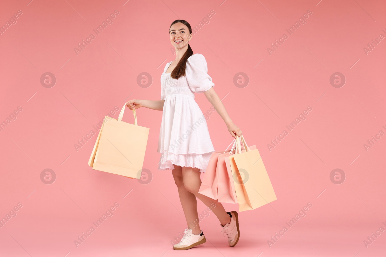 Positive woman with shopping bags on light pink background Photo of Positive woman with shopping bags on light pink background