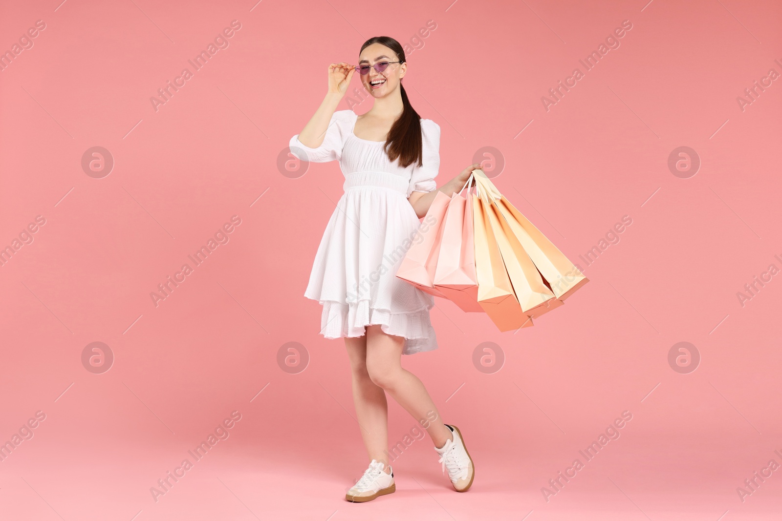 Positive woman with shopping bags on light pink background Photo of Positive woman with shopping bags on light pink background