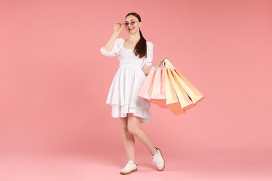 Photo of Positive woman with shopping bags on light pink background