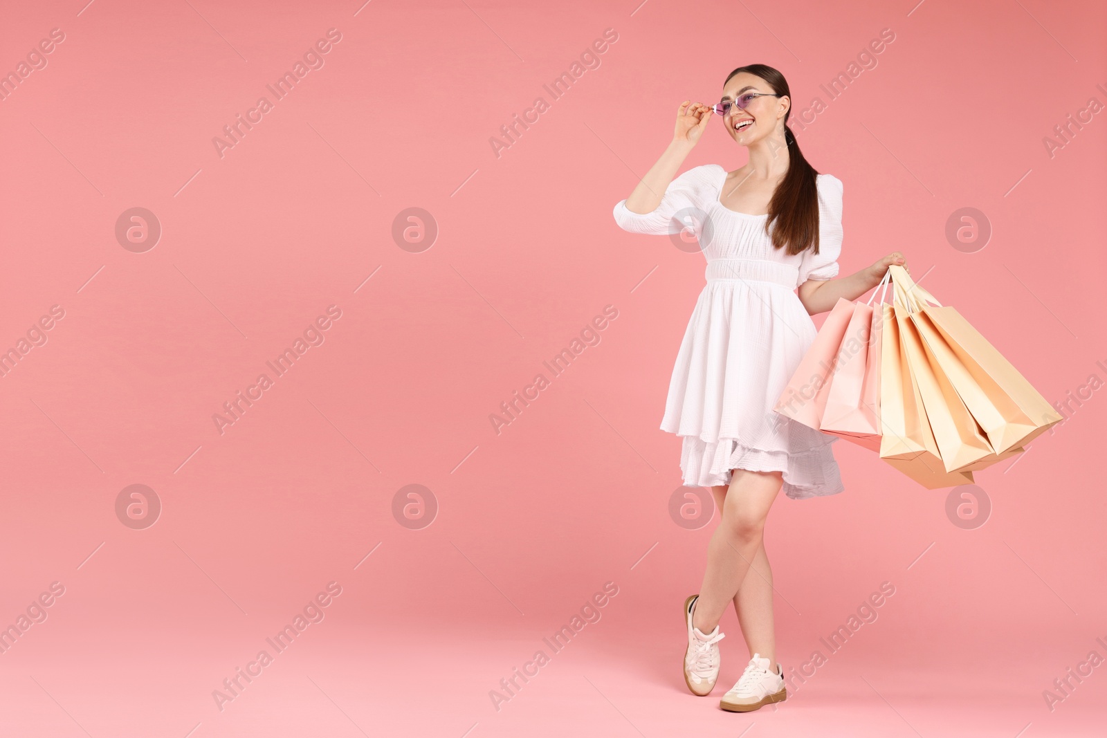 Positive woman with shopping bags on light pink background. Space for text Photo of Positive woman with shopping bags on light pink background. Space for text