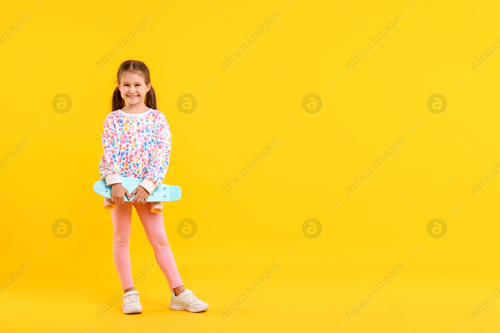 Little girl with penny board on yellow background, space for text Photo of Little girl with penny board on yellow background, space for text