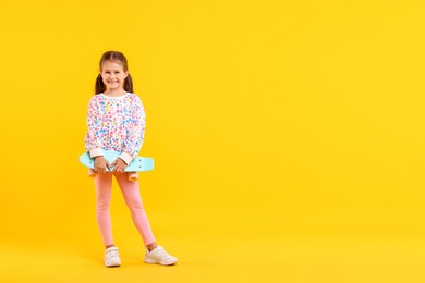 Photo of Little girl with penny board on yellow background, space for text