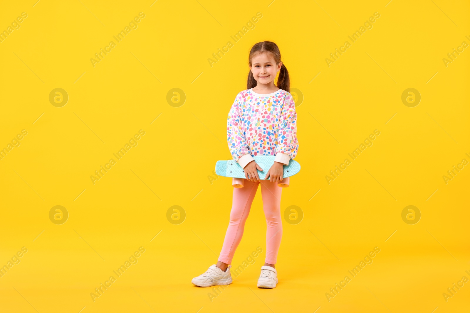 Little girl with penny board on yellow background Photo of Little girl with penny board on yellow background