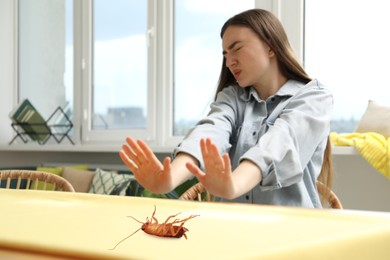 Image of Emotional young woman frightened by cockroach on table at home