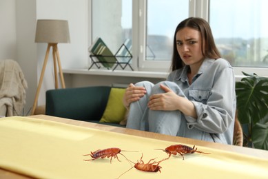 Image of Emotional young woman looking in disgust at cockroaches on table indoors