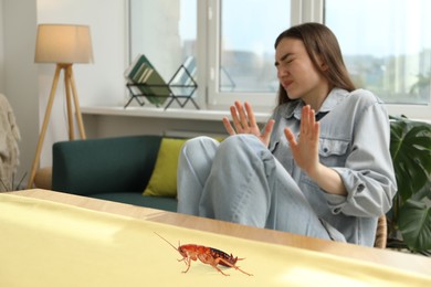 Image of Emotional young woman frightened by cockroach on table at home