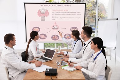 Image of Team of doctors using video projector during conference about thyroid hormones indoors. Illustrations on projection screen