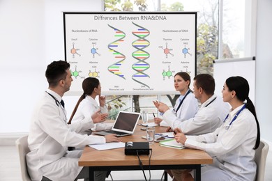 Image of Team of doctors using video projector during conference about DNA and RNA indoors. Illustrations on projection screen