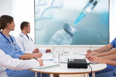 Image of Team of doctors using video projector during conference about DNA indoors. Illustrations on projection screen