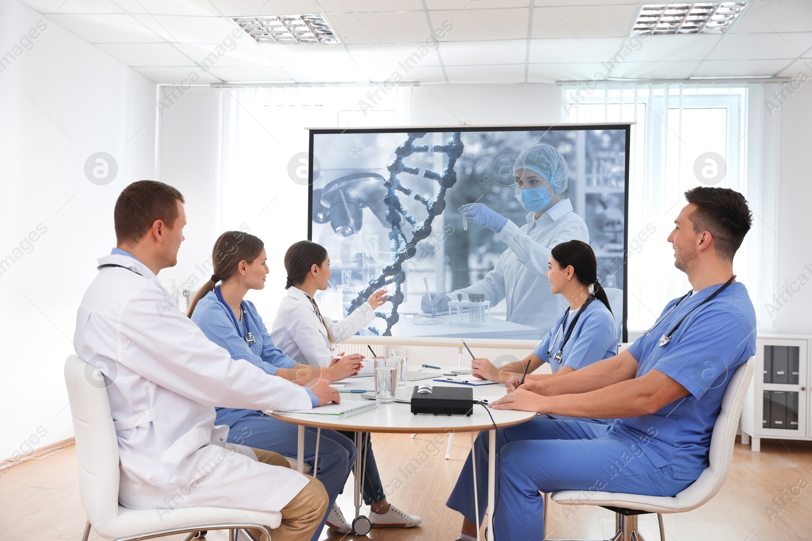 Team of doctors using video projector during conference about DNA indoors. Illustrations on projection screen Image of Team of doctors using video projector during conference about DNA indoors. Illustrations on projection screen
