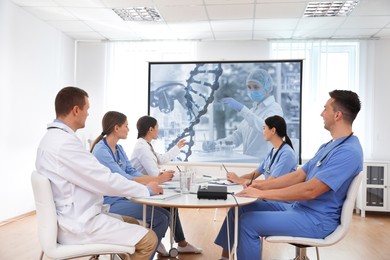 Image of Team of doctors using video projector during conference about DNA indoors. Illustrations on projection screen
