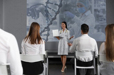 Image of Healthcare professional giving lecture about DNA in conference room using video projector. Illustration on projection screen