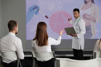 Image of Healthcare professional giving lecture about genetics in conference room using video projector. Illustrations on projection screen