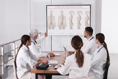 Image of Team of doctors using video projector during conference about scoliosis indoors. Illustrations on projection screen