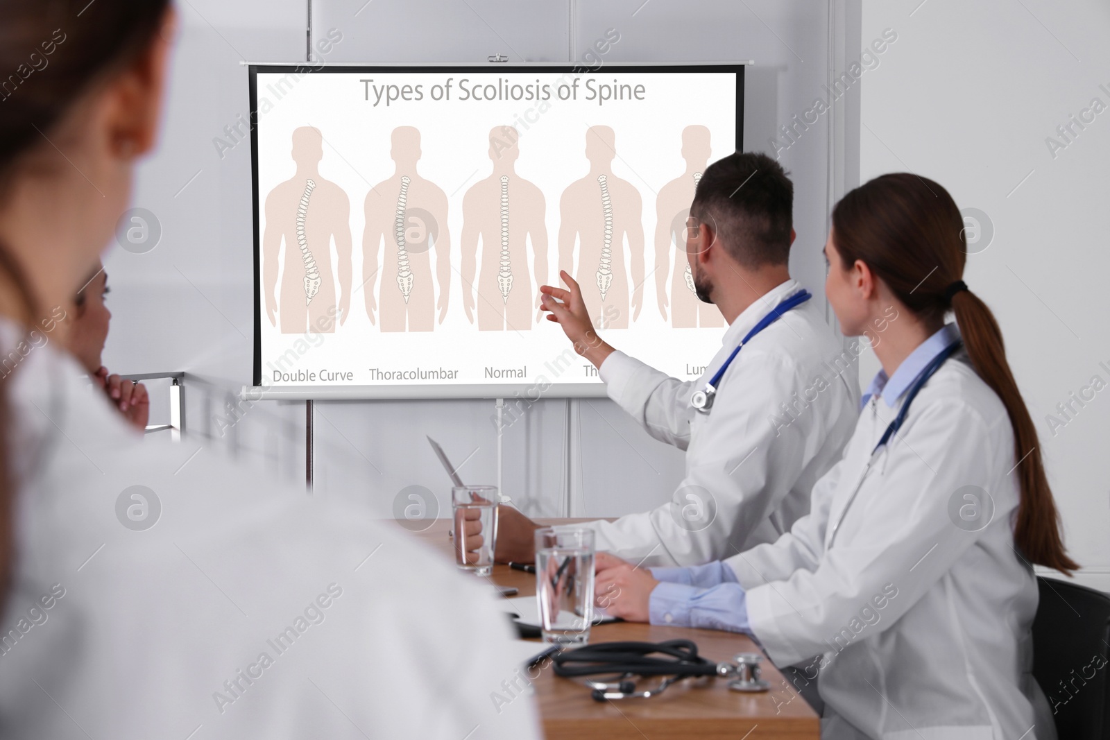 Team of doctors using video projector during conference about scoliosis indoors. Illustrations on projection screen Image of Team of doctors using video projector during conference about scoliosis indoors. Illustrations on projection screen