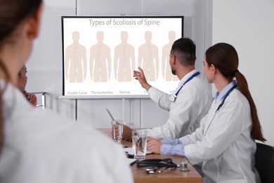 Image of Team of doctors using video projector during conference about scoliosis indoors. Illustrations on projection screen