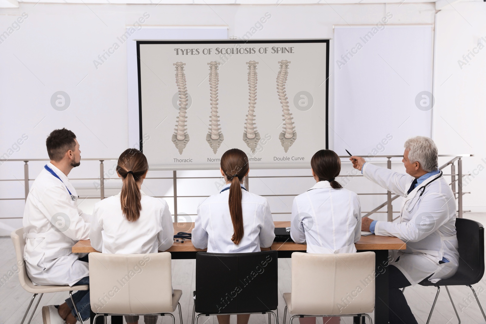 Team of doctors using video projector during conference about scoliosis indoors. Illustrations on projection screen Image of Team of doctors using video projector during conference about scoliosis indoors. Illustrations on projection screen