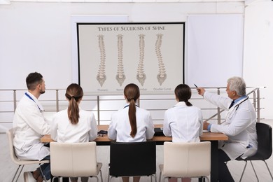 Image of Team of doctors using video projector during conference about scoliosis indoors. Illustrations on projection screen