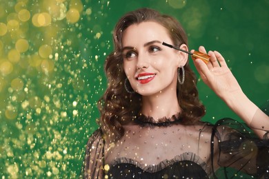 Image of Smiling woman applying mascara under falling glitter on green background, bokeh effect