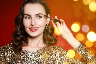 Image of Smiling woman applying mascara on red background with blurred lights, bokeh effect