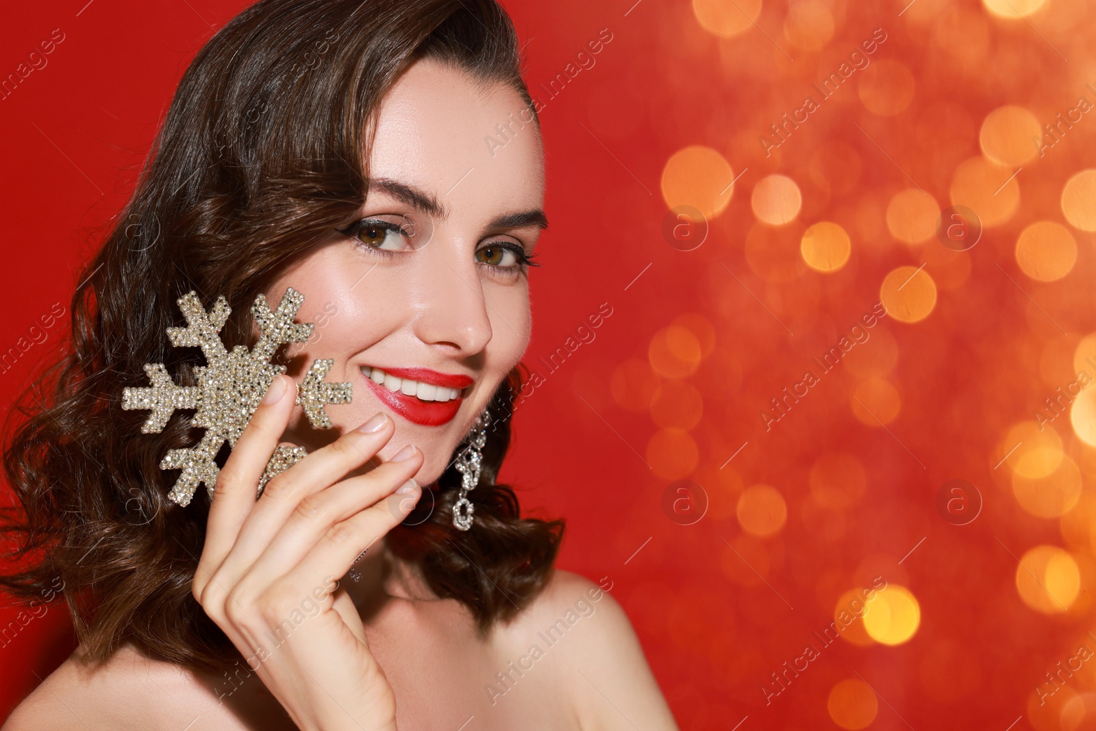 Smiling woman with perfect makeup holding decorative snowflake on red background, bokeh effect. Christmas celebration Image of Smiling woman with perfect makeup holding decorative snowflake on red background, bokeh effect. Christmas celebration