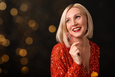 Image of Smiling woman with perfect makeup holding Christmas candy cane on black background, bokeh effect