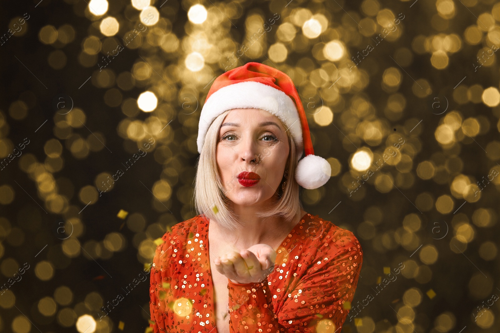 Woman with perfect makeup in Santa hat blowing confetti on black background, bokeh effect. Christmas celebration Image of Woman with perfect makeup in Santa hat blowing confetti on black background, bokeh effect. Christmas celebration