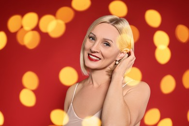 Image of Smiling woman with perfect makeup on red background, blurred lights. Bokeh effect