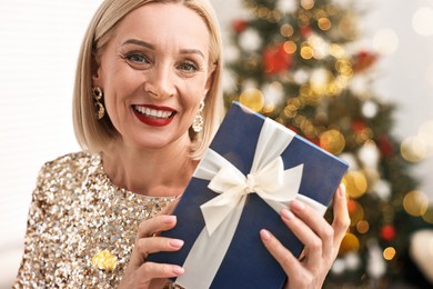 Image of Smiling woman with perfect makeup and Christmas gift at home, bokeh effect