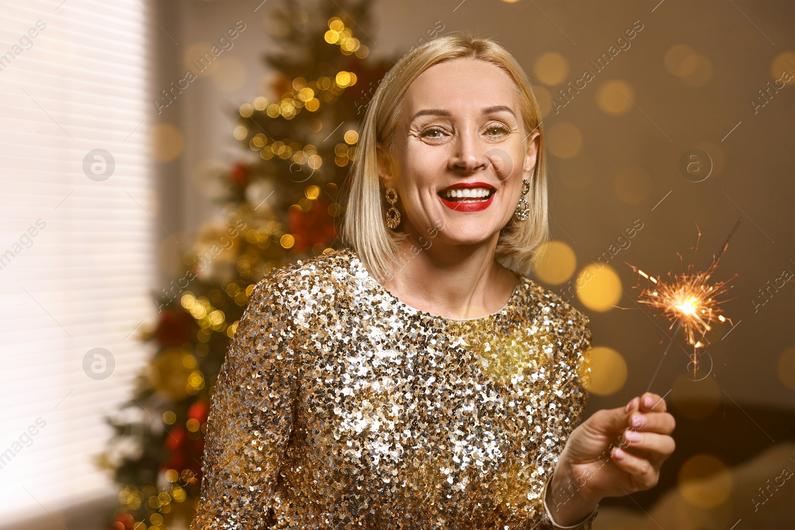 Smiling woman with sparkler celebrating Christmas at home, bokeh effect Image of Smiling woman with sparkler celebrating Christmas at home, bokeh effect