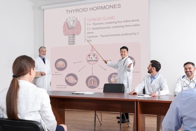 Image of Healthcare professionals giving lecture about thyroid hormones in conference room using video projector. Illustrations on projection screen