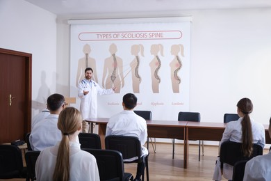 Image of Healthcare professional giving lecture about scoliosis in conference room using video projector. Illustrations on projection screen