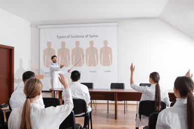 Image of Healthcare professional giving lecture about scoliosis in conference room using video projector. Illustrations on projection screen