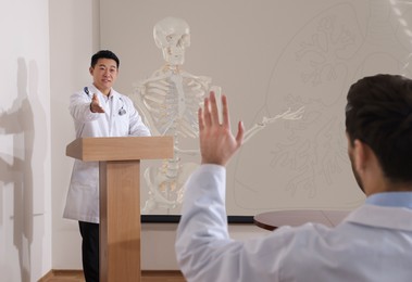 Image of Healthcare professional giving lecture about in conference room using video projector. Human skeleton model on projection screen