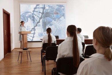Image of Healthcare professional giving lecture about DNA in conference room using video projector. Illustrations on projection screen