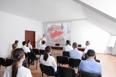 Image of Healthcare professional giving lecture about liver in conference room using video projector. Illustration on projection screen
