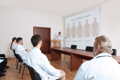 Image of Healthcare professional giving lecture about scoliosis in conference room using video projector. Illustrations on projection screen