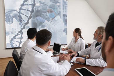 Image of Team of doctors using video projector during conference about DNA indoors. Illustrations on projection screen